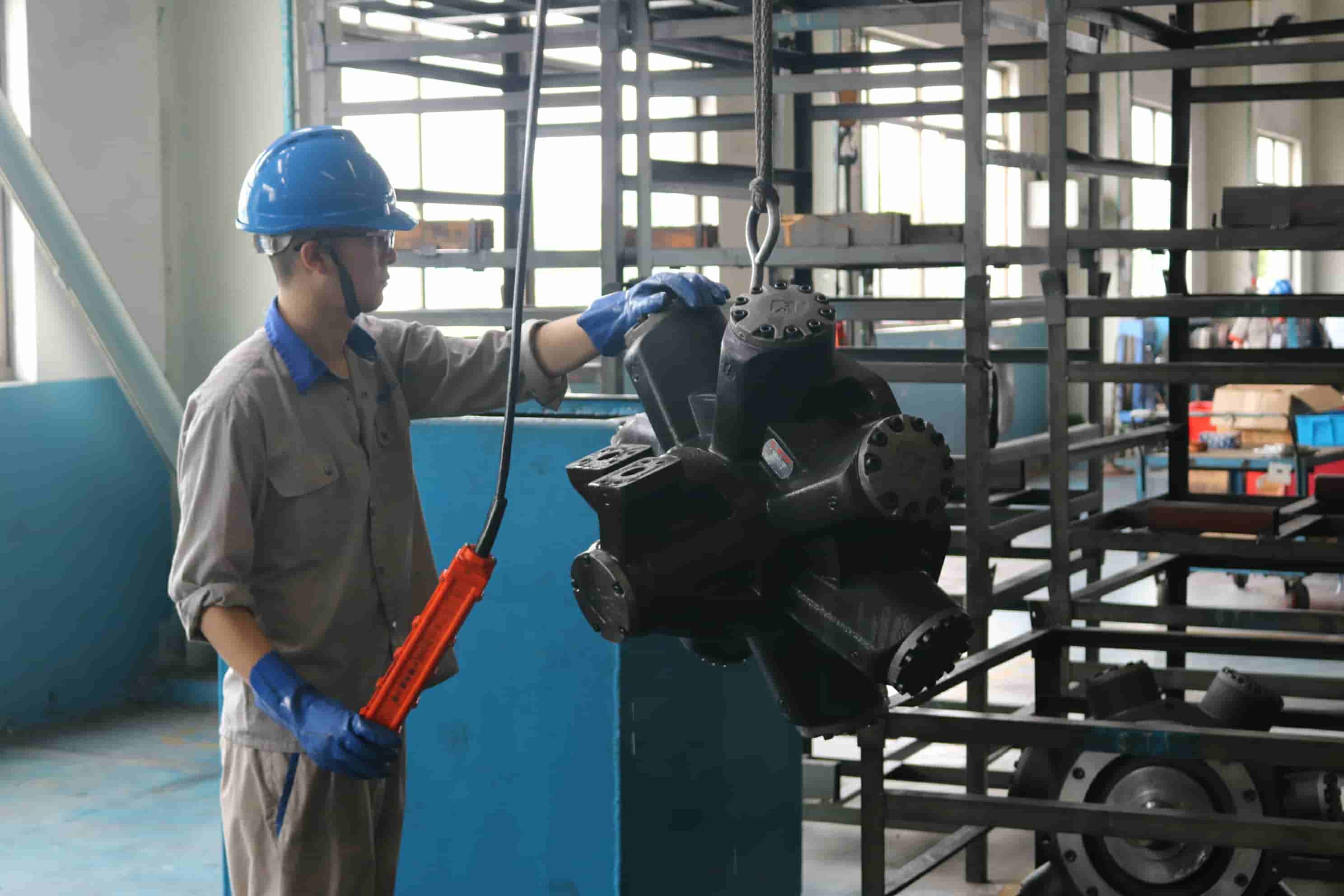 Blince worker lifting a heavy-duty hydraulic travel motor during factory assembly